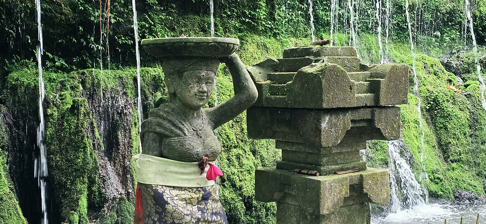Stone woman statue balancing a tray beside mossy fountain blocks and cascading waterfalls in a lush green temple garden.