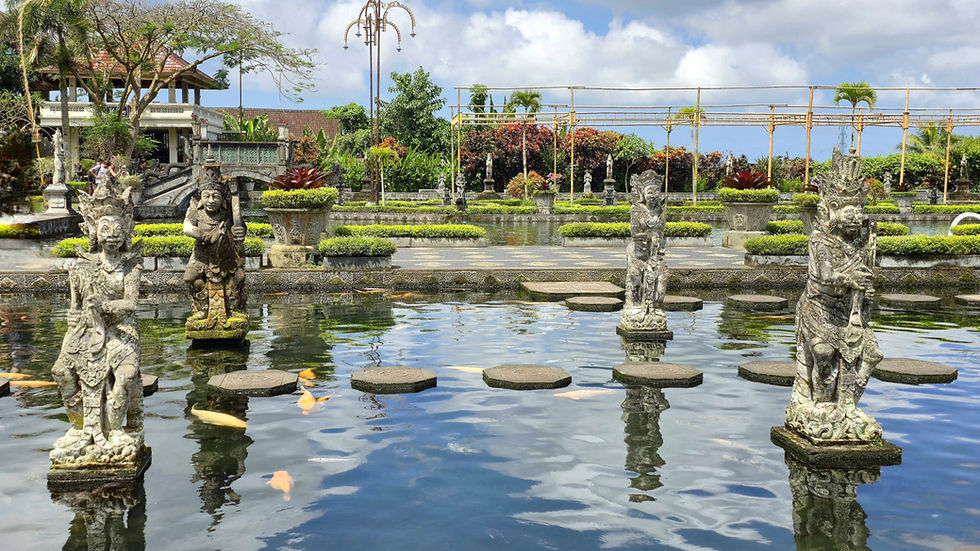 Stone statues on water with stepping stones, lush garden background, vibrant foliage, and a cloudy sky create a serene, elegant scene.