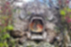 Ornate wooden sculpture of a mythical creature with wide eyes and open mouth, surrounded by lush greenery and red flowers, exudes a mystical aura.