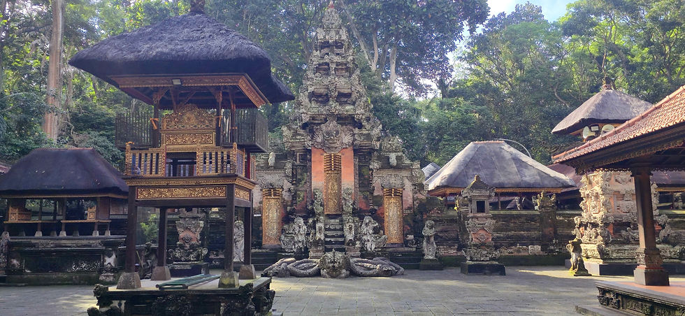 Ancient temple courtyard with intricate stone carvings and thatched-roof pavilions surrounded by lush green trees, under a clear sky.