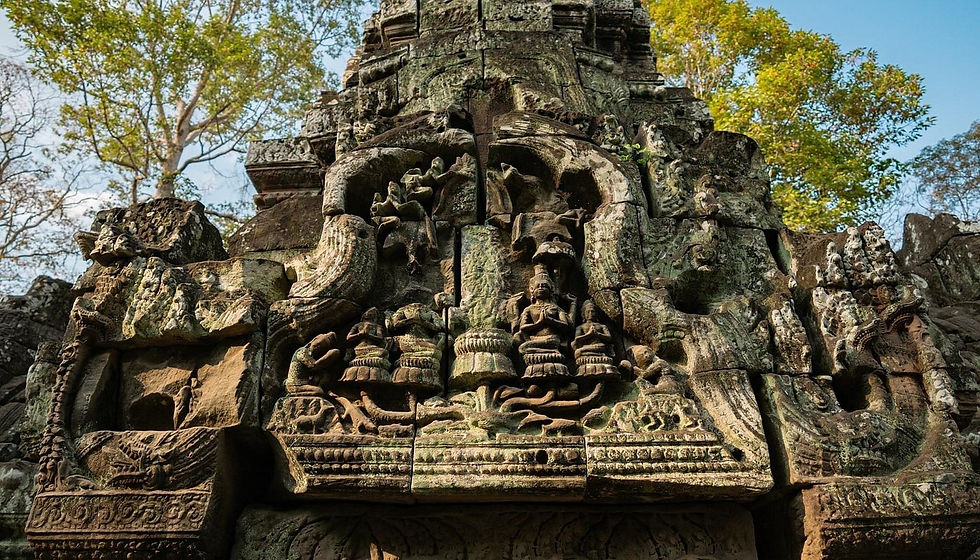Ancient stone temple carvings with intricate patterns and figures, set against a backdrop of green trees and a clear blue sky.