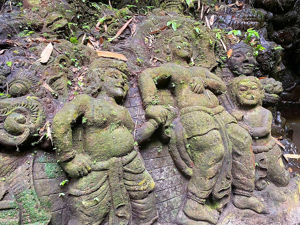 Ancient stone relief of figures with intricate carvings, covered in moss and foliage, creating a serene, weathered atmosphere in nature.