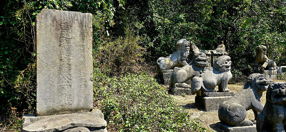 Ancient stone tablet with carved text stands beside stone lion statues amidst lush greenery, creating a serene, historical atmosphere.