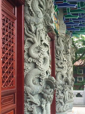 Stone dragon carvings adorn a temple entrance, featuring intricate details. The background includes wooden lattice doors and colourful eaves.
