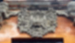 Ornate stone carving of a fierce face with floral details on a red brick temple background, conveying a majestic and ancient feel.