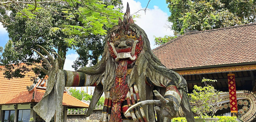 Intricate Balinese statue with vibrant red, black and white colours stands in a lush garden setting, under a clear blue sky.