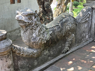Stone dragon sculpture in a garden setting, detailed carvings and aged texture. Sunlight casts shadows on the stone pathway beside it.
