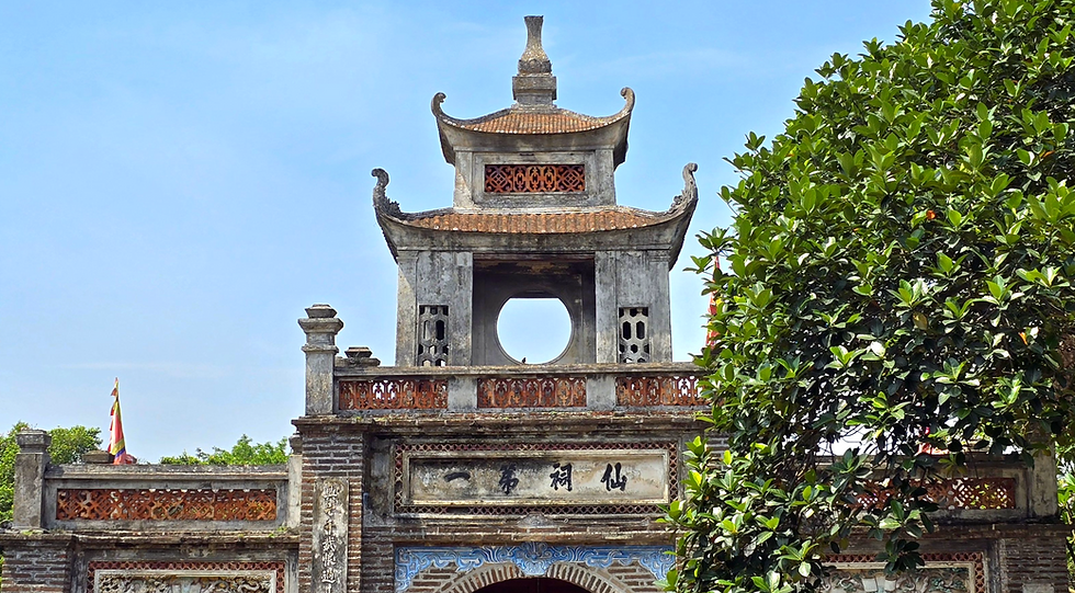 Ornate stone temple gate with pagoda-style roof, intricate carvings, and Chinese characters, set against clear sky and lush greenery. Peaceful mood.