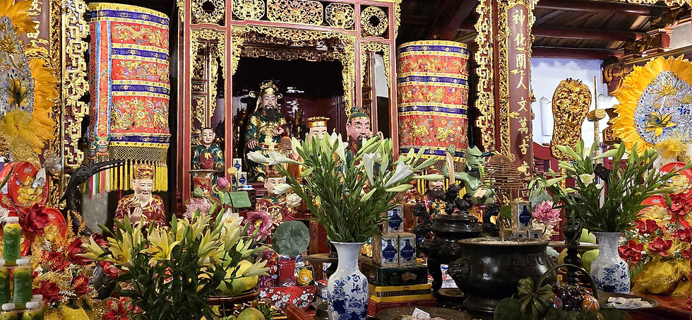 Colourful altar with statues and offerings, including lilies in vases, ornate gold patterns, and bright banners. Serene, vibrant temple scene.