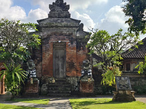 Serene Balinese temple courtyard with a stone path, lush trees, and an ancient brick gate under a bright cloudy sky.