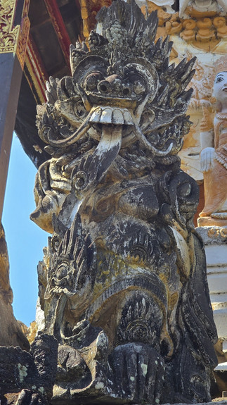 Weathered black stone guardian demon statue with tusks and ornate carvings on a temple facade under blue sky.