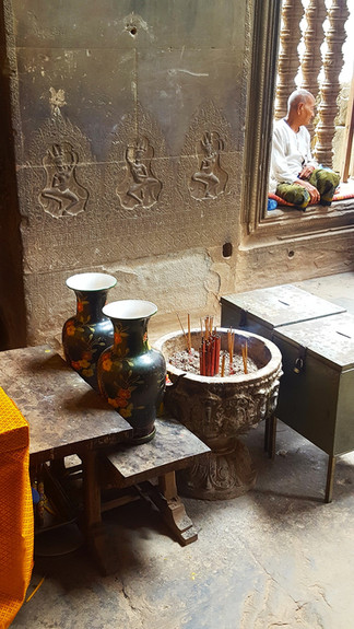 golden pot full of incense sticks, local man sitting in the window sill, ornate but faded carvings on the walls