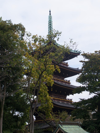 5 tiered timber shrine with green roof and spire, partially obscured by tall green trees