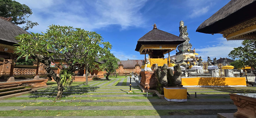 Lush temple courtyard with ornate stone structures, yellow draped altar, and a frangipani tree under a vibrant blue sky. Peaceful ambiance.