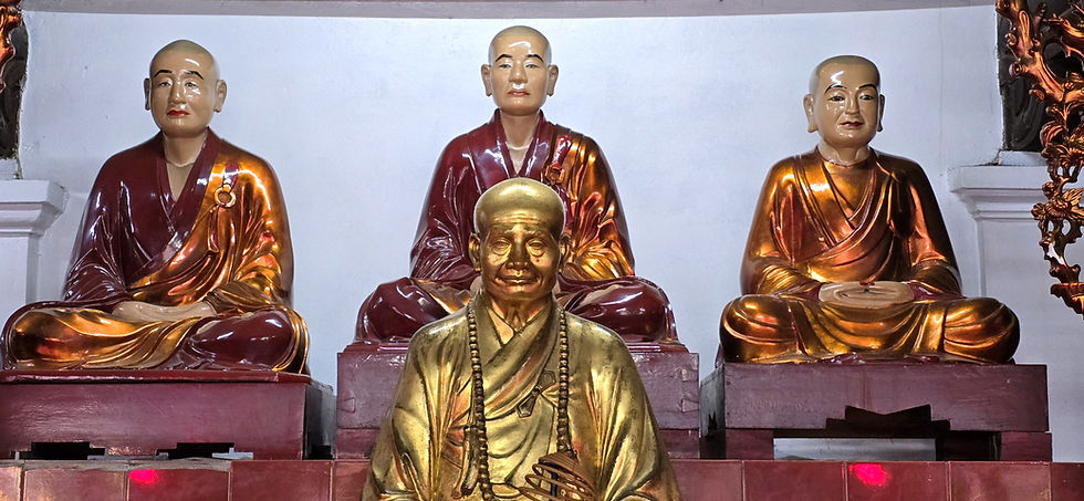 Golden statues of monks seated in meditation, with serene expressions, on a red pedestal in a dimly lit temple setting.