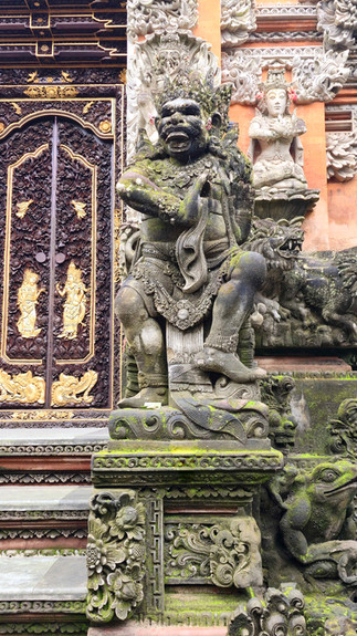Ornate stone sculpture of a mythical figure with intricate carvings, moss-covered texture, and a decorative entrance door in the background.