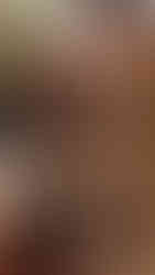 Close-up of a detailed, weathered wooden face sculpture with deep-set eyes and a prominent brow in a dimly lit setting. Earthy tones.