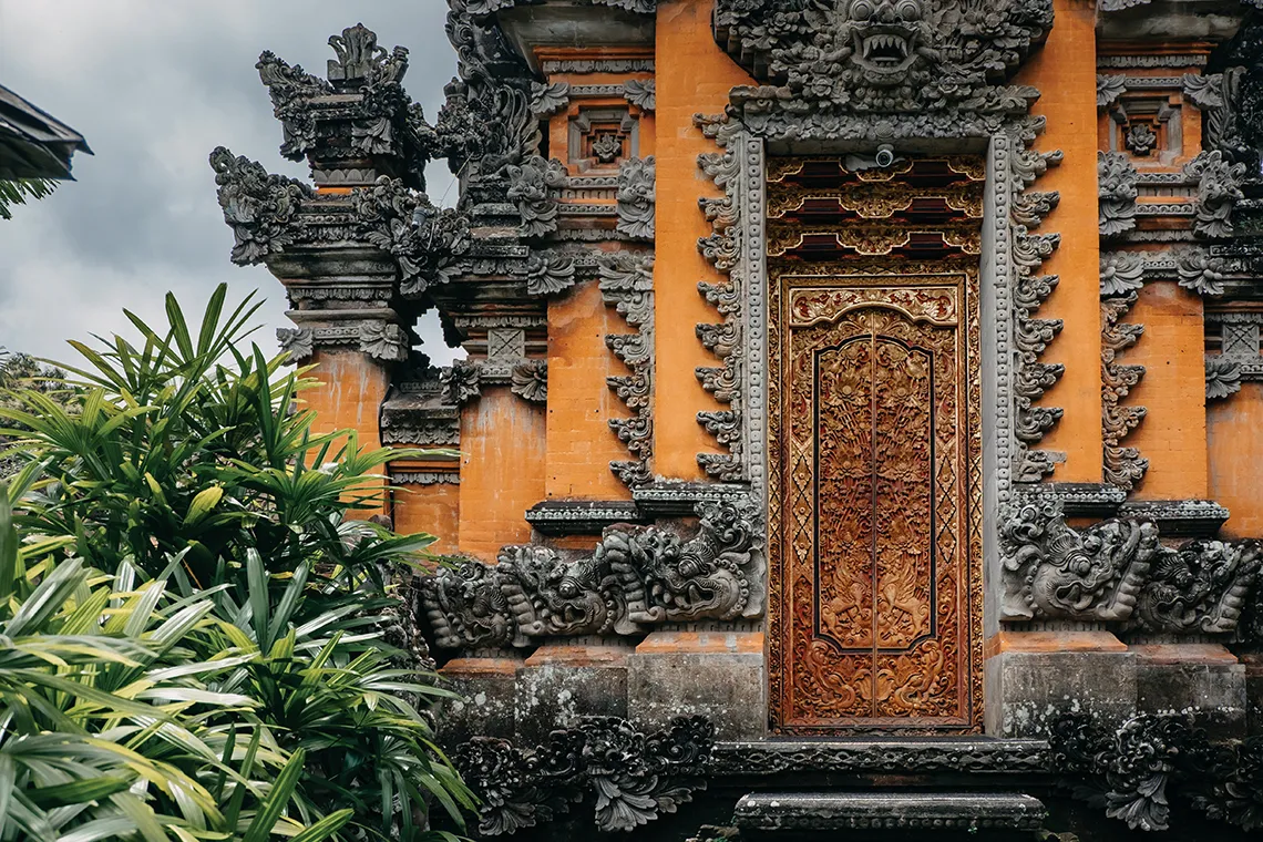 close-up of orange temple gate with heavily carved grey stone trim, green leaves 