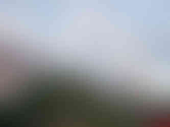 Buddha statue sits serenely on a hill under a cloudy sky, surrounded by lush green trees and distant mountains in the background.