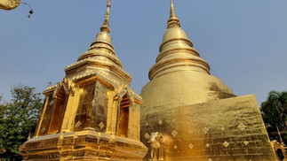 Golden pagoda and chedi under a clear blue sky, adorned with intricate details. Green trees surround the structure, creating a serene atmosphere.