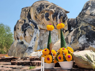 A closeup of the reclining Buddha's face at the time of his death as he enters Nirvana, behind 2 bowls of offerings filled with orange marigolds
