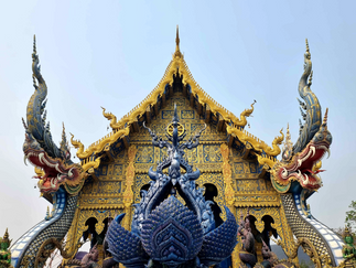 The vivid blue exterior of Wat Rong Suea Ten temple in Chiang Rai, adorned with gold trim, naga serpents, and intricate carvings along the roofline