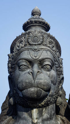Close-up of a stone Hanuman statue with intricate carvings against a clear blue sky, conveying a serene and powerful presence.
