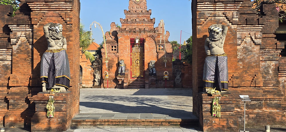 Balinese temple gate with two stone guardian statues in black-and-white cloth, sunlit brick courtyard, and ornate carved doorway