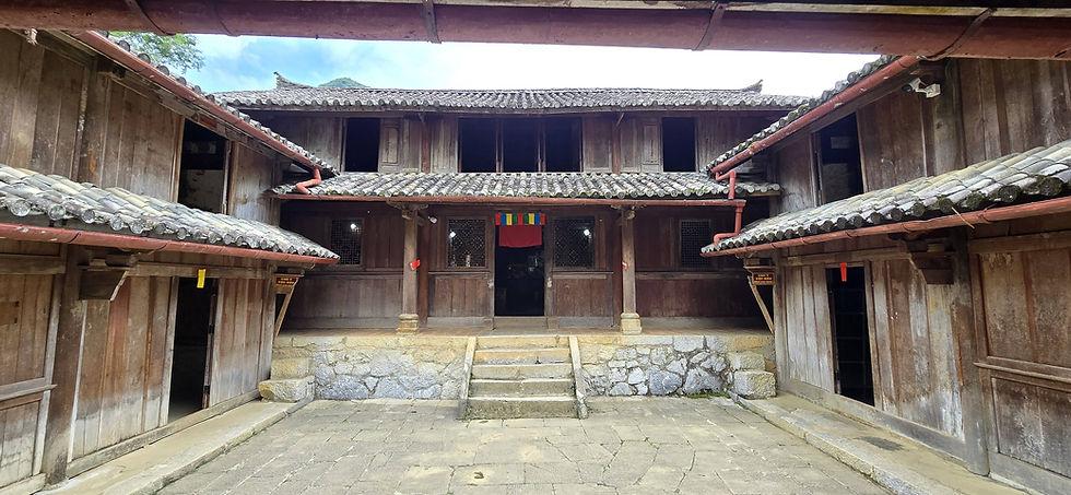 Wooden courtyard with stone steps leading to a rustic building. Tiled roofs, colourful flag, and a serene, traditional atmosphere.