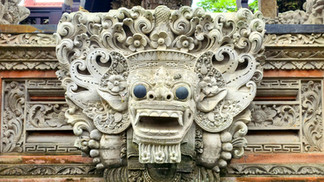 Ornate stone carving of a mythical creature with bulging eyes and intricate floral designs. The background features elaborate patterns.