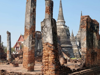 Ancient brick ruins with tall columns and distant pagodas in a historic site under a clear blue sky, exuding a serene and timeless aura.
