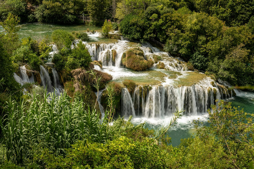 Lush green landscape with cascading waterfalls surrounded by dense foliage. Clear water flows energetically, creating a serene, natural scene.
