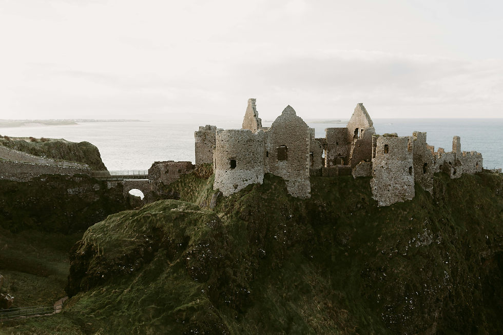 Ancient stone castle ruins on a green cliff by the sea under a cloudy sky, evoking a historic and serene atmosphere.