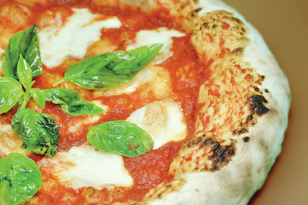 Close-up of a margherita pizza with fresh basil leaves, melted cheese, and a crispy golden crust on a brown background.