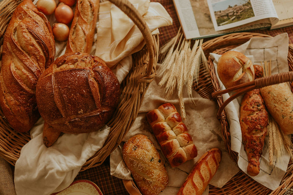 Assorted bread loaves and baguettes in wicker baskets, surrounded by onions and wheat stalks. Warm, rustic setting with open cookbook.