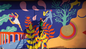 Zoe Power stands on a ladder making finishing touches to a huge mural co-designed and collaboratively painted with the community as part of Art Eat Festival