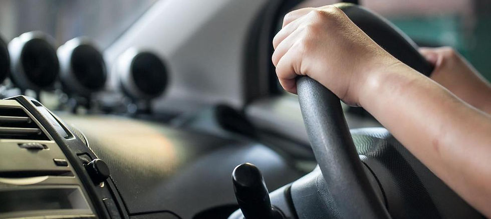 La imagen muestra una vista en primer plano de una persona agarrando un volante dentro de un automóvil. El enfoque está en las manos que sujetan el volante, con el tablero de instrumentos y algunos indicadores visibles en el fondo. Esta imagen es relevante ya que representa la acción de conducir y la importancia de mantener un agarre adecuado en el volante para la seguridad y el control del vehículo.