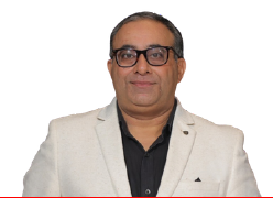 Portrait of a smiling man in glasses wearing a light beige blazer over a black shirt against a white background