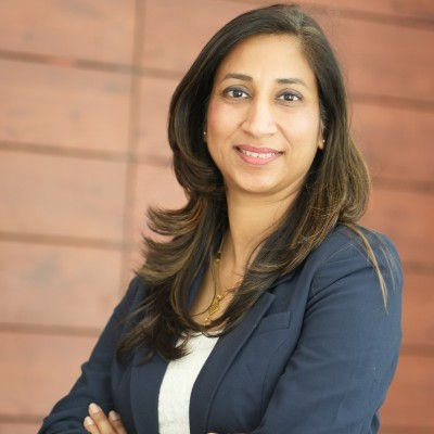 Smiling woman in a navy blazer poses with arms crossed against a blurred wooden wall.