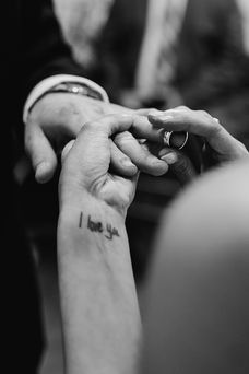 A close up black and white image of the bride placing a wedding band on the groom's finger.