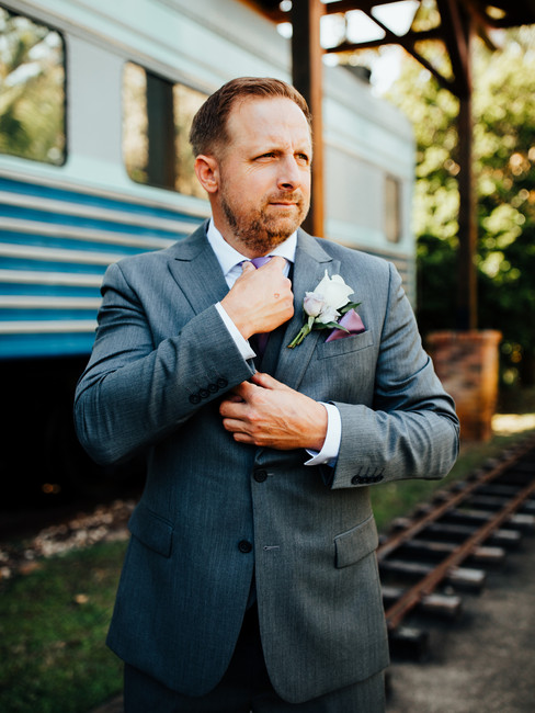 groom stands next to train straightening tie