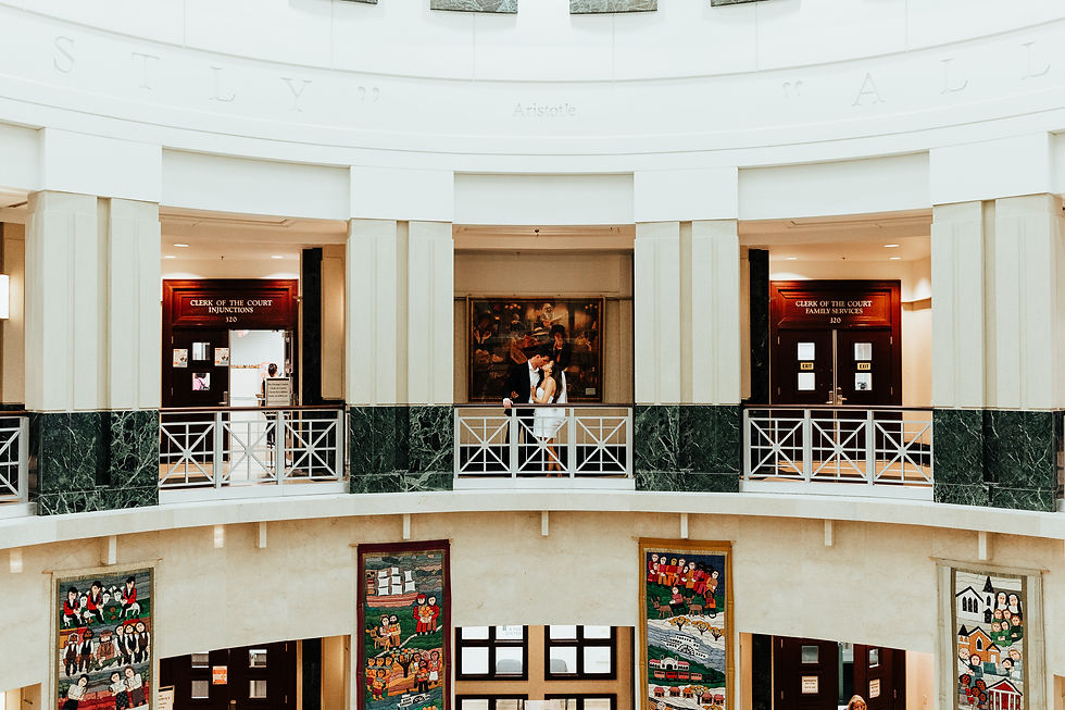 Couple embraces on an upper floor of a courthouse, with art and "Clerk of the Court" signs visible. Elegant architecture and a romantic mood.