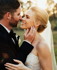 a bride and groom gently touch noses together while smiling at each other while standing in golden light