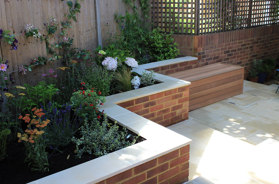 A-zig-zag-shaped-brick-wall-with-sawn-sandstone-copping-stones-in-a-paved-small-city-garden