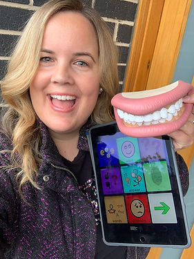 This is a photo
 of the founder of speech for the stars, Felicity Conlan. She is smiling and holding a mouth anatomy model and an AAC device.