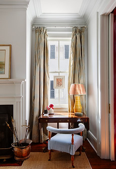 Wooden desk and blue plush chair with an elevated design situated in front of a window