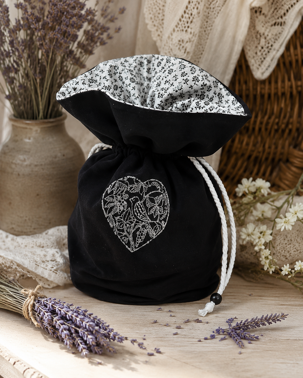 Sac bourse brodé Oiseau en coton noir doublé présenté dans une décoration naturelle.