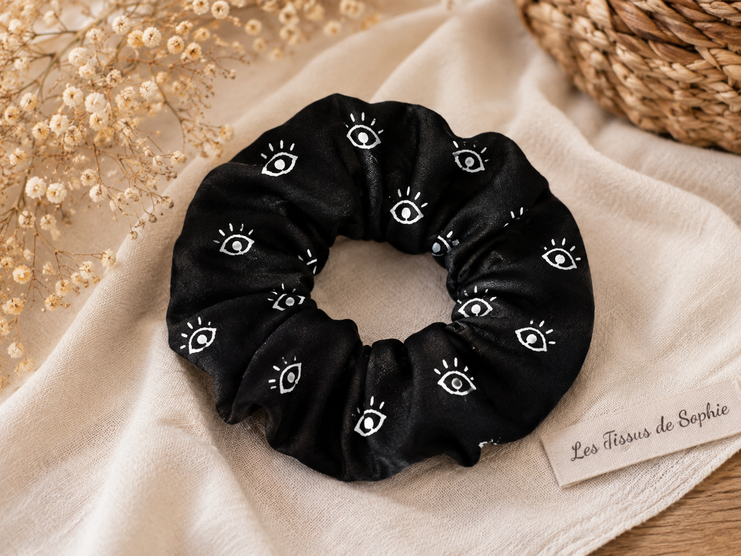 Chouchou noir en polyester à motif œil blanc présenté dans une ambiance chaleureuse.