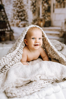 Smilende baby ligger på et mykt hvitt teppe under julefotografering i studio i Fredrikstad.