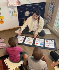 Teacher guiding children through a learning activity on the floor.